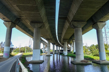 Underside of a large concrete highway overpass or elevated roadway crossing over the Moonee Ponds Creek in Melbourne, Australia. Concept of urban infrastructure, waterway management, civil engineering © Doublelee