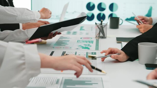 A diverse team of professionals engages in a collaborative business meeting, analyzing data charts on laptops and documents, fostering strategic insights and teamwork. SACTR