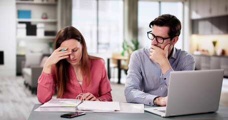 Young couple sitting in kitchen stressed about financial troubles and bills