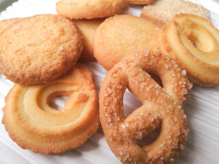 Close-up of assorted golden butter cookies with sugar sprinkles, arranged on a white surface.