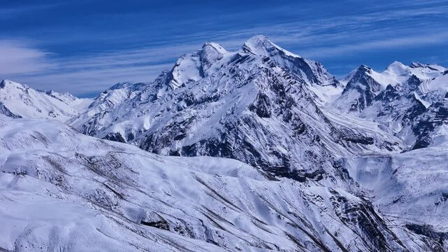 Aerial drone shot capturing the grandeur of the winter-clad Himalayan mountains, their icy peaks standing tall against the clear blue sky.