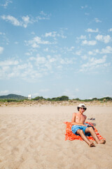 Jeune homme adolescent sur une plage de sable fin. Homme torse nu et bermuda sur la plage de Pals avec l'antenne de la CIA en arri&egrave;re plan. Jeune gar&ccedil;on bronzant &agrave; la plage. Vacances &agrave; la mer.