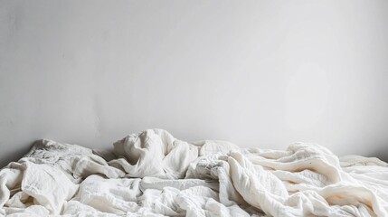 Obraz premium Messy, white linen bedding against a plain wall. Soft, unmade bed