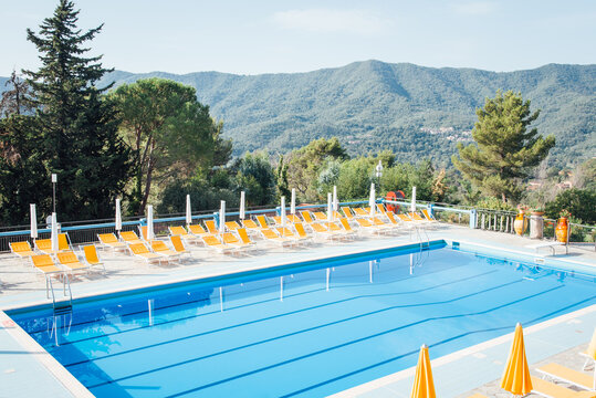 Piscine dans un camping en Italie. Grande piscine bleue, parasols et transats jaunes, paysage de montagne. Personne. Absence de clients. Pas de touriste. Vacances en Italie