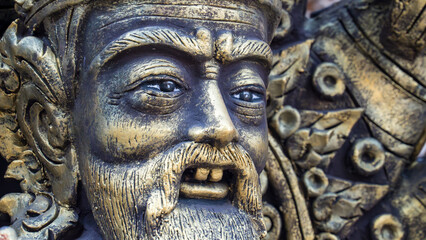 Close-up of an ornate golden guardian statue with an expressive face in Thailand