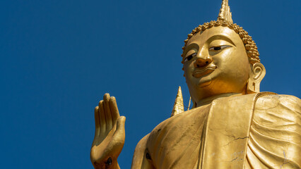 Golden standing Buddha statue with raised hand against blue sky in Thailand