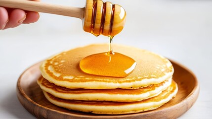 Hand pouring honey from a wooden dipper onto warm pancakes, delicious and mouthwatering breakfast scene
