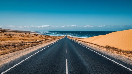 Fototapeta premium Endless desert road meeting ocean under clear blue sky