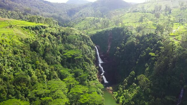 Aerial drone of Moray Waterfall flowing into the lake among the hills with green tea. Sri Pada falls. Maskeliya, Sri Lanka.