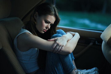 A young woman of Caucasian descent sits in a car, showing emotions of sadness and reflection while...