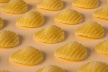 Background pasta . Side view of isolated a raw Italian durum wheat orecchiette pasta on a light orange background .