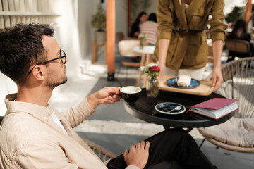 A man relaxes with a cup of coffee at an outdoor cafe as a server brings him food. The sunny ambiance and casual setting create a serene and inviting atmosphere.