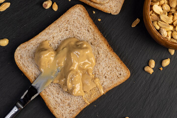 Fototapeta premium peanut butter on a piece of bread and roasted peanuts on the table