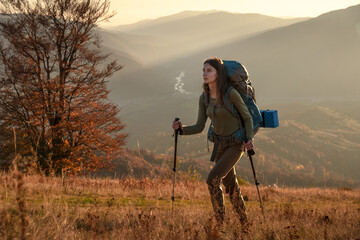 Young woman hiking in the mountains at sunset, carrying a backpack. Scenic outdoor adventure