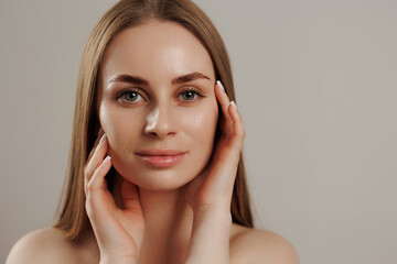 Woman with long hair elegantly touching her face in a neutral backdrop during a beauty session