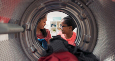 A mother sits by the washing machine with her daughter, both of them smile as they load colorful...