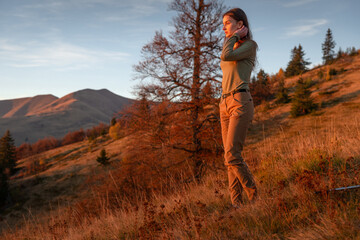 Naklejka premium Beautiful female hiker adjusting her hair while standing in a scenic mountain meadow at sunset.
