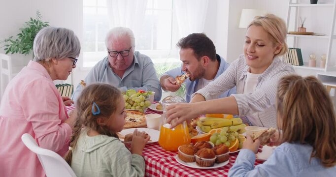 Happy big multi generation family sitting around table full of different food, eating pizza during dinner. Cheerful parents, grandparents and children enjoying meal together. Family bonds concept.