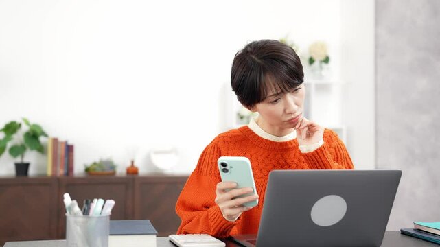 スマホとノートパソコンを見ながら悩むミドル女性