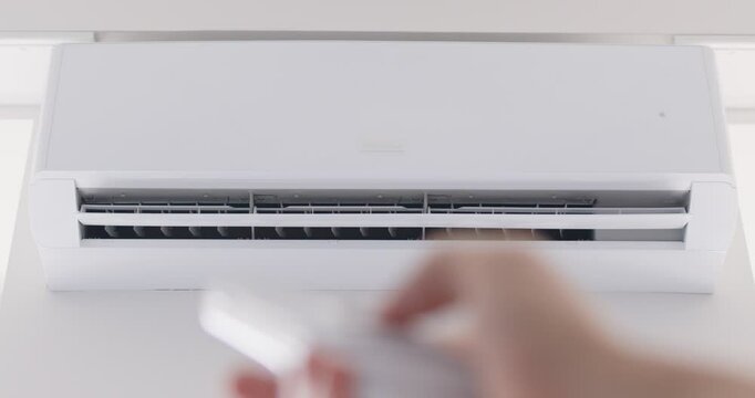 Close up cropped shot of person hand using remote control, adjusting temperature and turning off air conditioning system at home. Comfort in managing indoor climate during changing weather conditions.