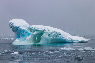 Sculptured Iceberg floating near the Antarctic Peninsula. Blue ice. Smaller chunks of ice in...