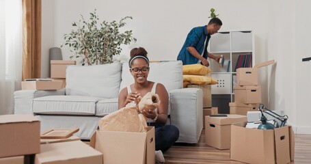 A cheerful wife sits on the floor in her new house and pulls a wooden photo frame from a box. She...