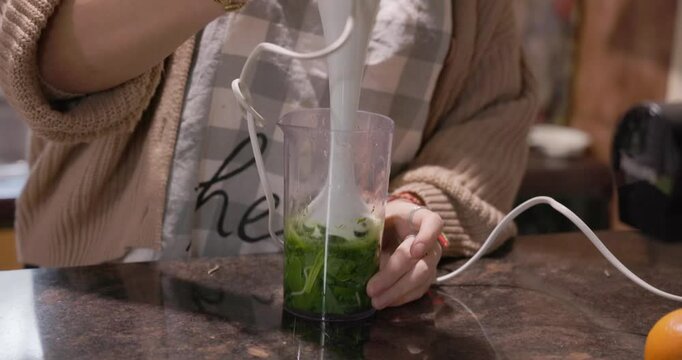 A young woman is blending a wild bear garlic in a kitchen