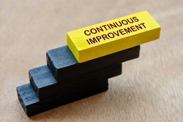 Continuous Improvement text on yellow wooden block stacking on other black wooden blocks....
