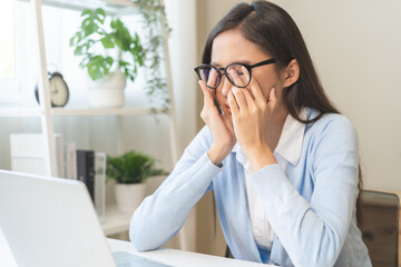 Exhausted, stressed asian young business woman working, wearing glasses, massage nose from dry eyes, suffer on work hard while use laptop computer at office home. Overtime job, debt problem people.