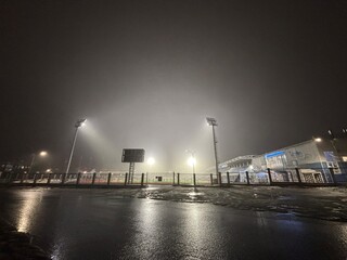 The football stadium is illuminated by lanterns during soccer practice at night during fog	