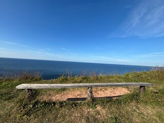 wooden bench on a cliff in summer, you can see the horizon and the blue sky with the sea