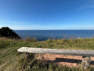 wooden bench on a cliff in summer, you can see the horizon and the blue sky with the sea