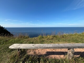 wooden bench on a cliff in summer, you can see the horizon and the blue sky with the sea