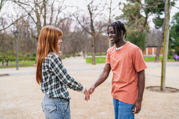 Fototapeta premium Young multiracial couple holding hands and smiling in park