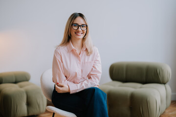 Obraz premium Professional woman smiles while seated in a stylish interior during daytime, showcasing modern decor and natural lighting