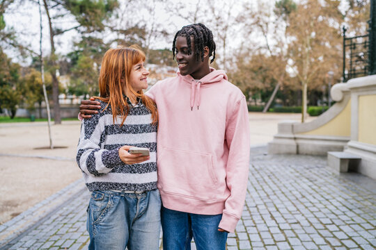 Young multiracial couple smiling and walking in park - Powered by Adobe