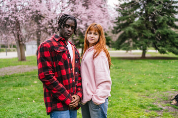 Obraz premium Young multiracial couple standing in park during cherry blossom season