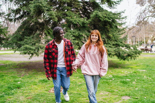 Happy multiracial young couple walking in park holding hands