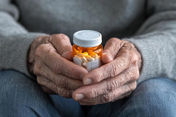 Senior person holding a bottle of medication while seated indoors in a cozy environment