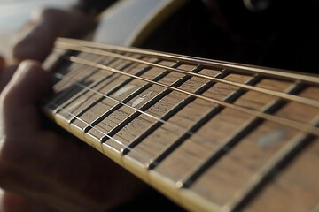 Fototapeta premium Close up view of fingers positioning on guitar fretboard during a sunlit music session outdoors