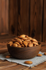 Raw almonds spilling from bowl, resting on small linen cloth napkin atop rustic wooden table, creating warm and inviting atmosphere perfect for healthy snacking
