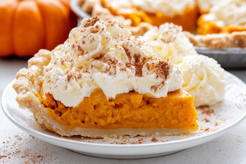 Slice of pumpkin pie topped with fluffy whipped cream and sprinkled with cinnamon in a cozy kitchen setting