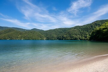 Obraz premium Serene lake nestled between green hills under a bright, cloudy blue sky