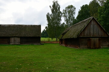 Obraz premium A close up on an old wooden shack, hut, or shelter surrounded by lush flora being a part of the garden, a wooden fence, and located next to a vast meadow, pastureland, or field seen in Poland