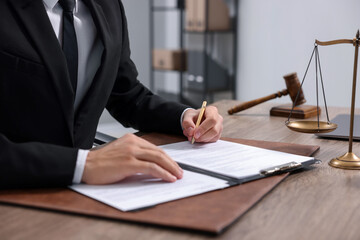 Notary signing document at wooden table in office, closeup