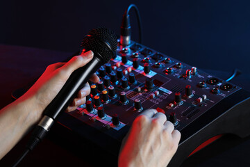 Woman holding microphone while working with professional mixing console at table, closeup