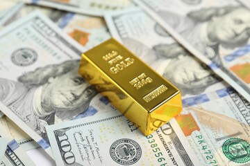 Fototapeta premium One shiny gold bar on dollar banknotes, closeup