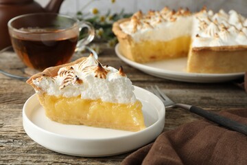 Piece of delicious pie with browned meringue and fork on wooden table, closeup