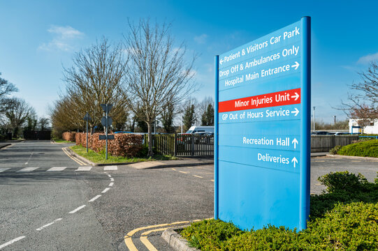 Large blue patient and visitor information and parking sign seen within the campus of a typical NHS hospital in Britain. The red sign is for the Minor Injury department.