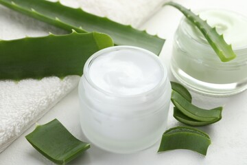 Moisturizing cream with extract of aloe vera, cut leaves and towel on white textured background, closeup